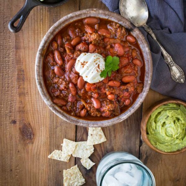 Instant pot chili in a bowl with guacamole and glass of water on the side