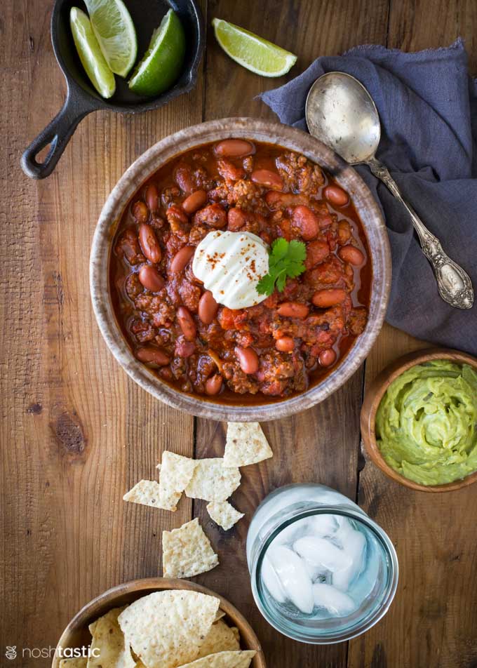 Instant pot chili in a bowl with guacamole and glass of water on the side