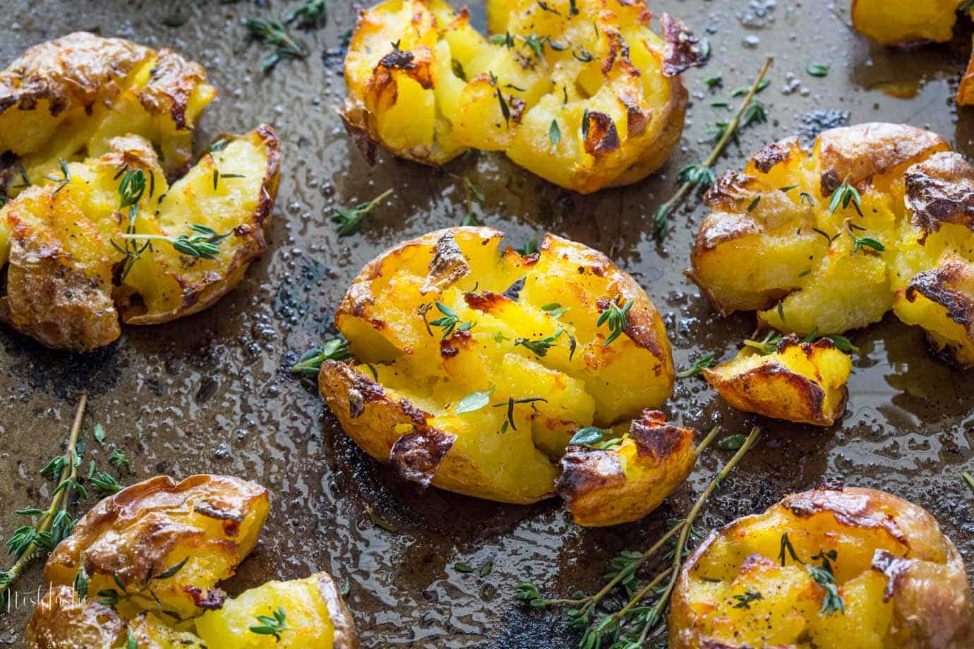 Smashed Potatoes baked with garlic, olive oil and herbs, fluffy in the middle and truly crispy on the top!! find out how to make them on noshtastic.com!! | paleo, gluten free, vegan, whole30, healthy recipe, side dish. baked potato, roasted potato.