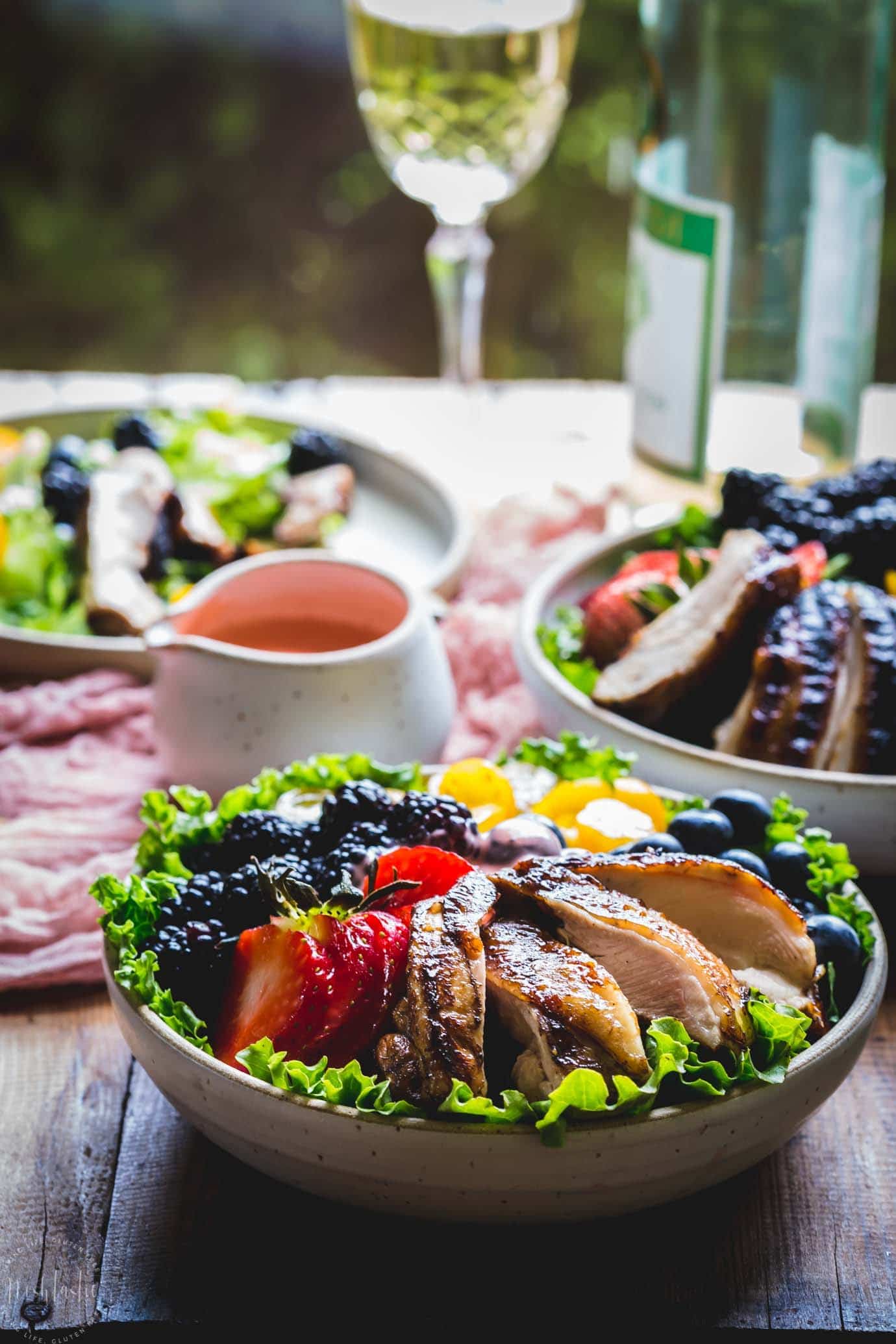 Grilled Balsamic Chicken Salad With Strawberry Vinaigrette and a glass of wine on a table