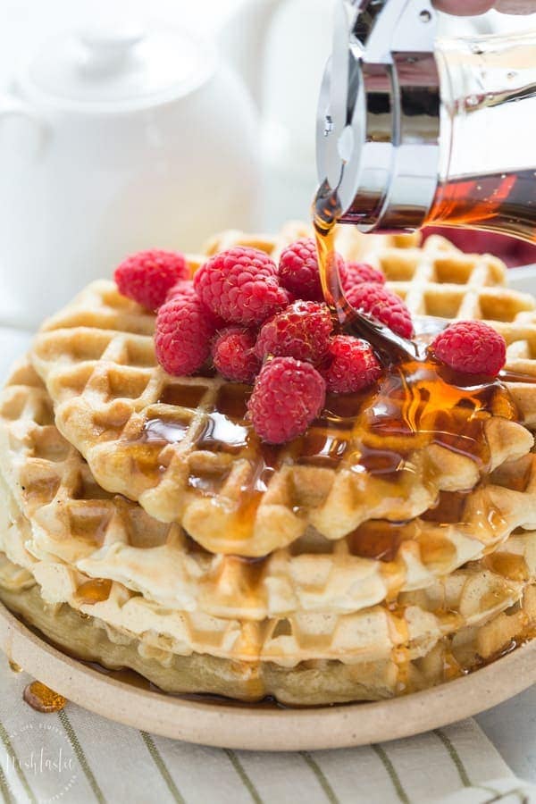 Plate of Gluten Free Waffles with raspberries and maple syrup poured over the top.