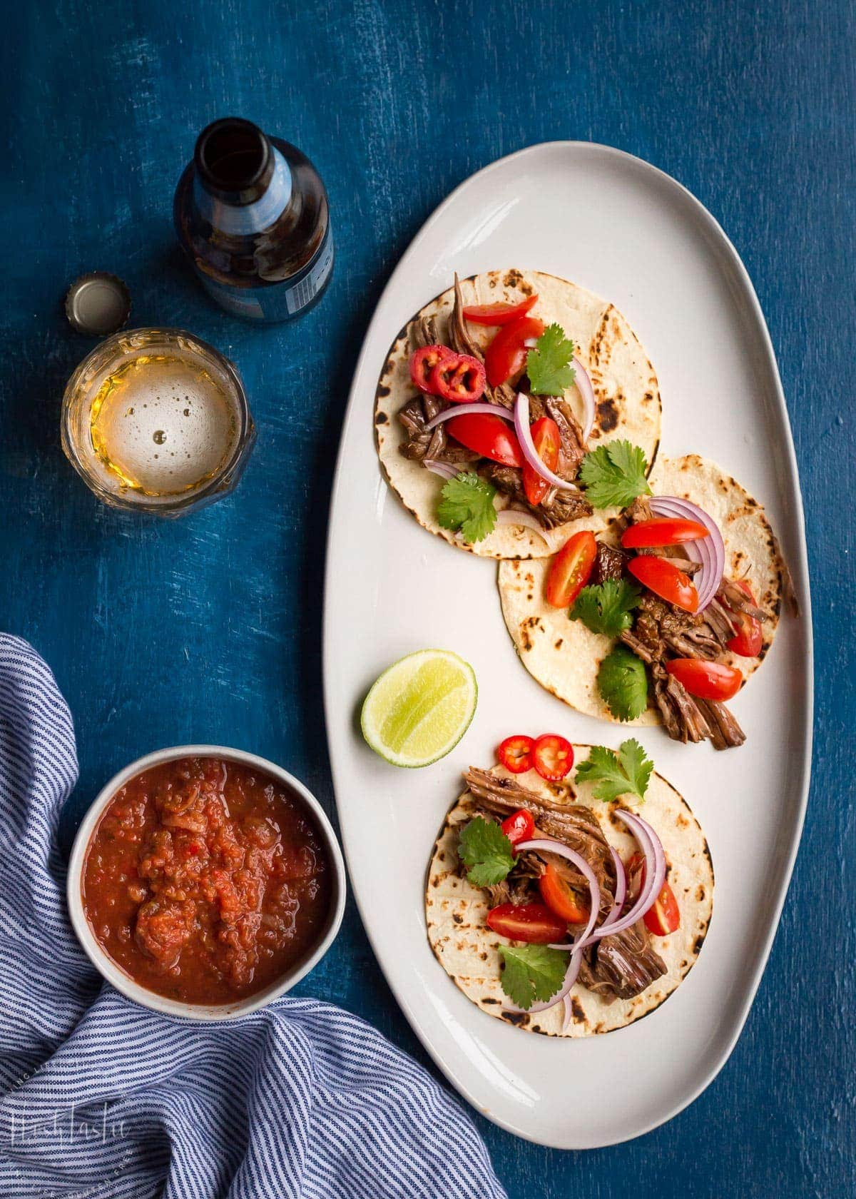 Salsa, cider and three beef tacos on a plate