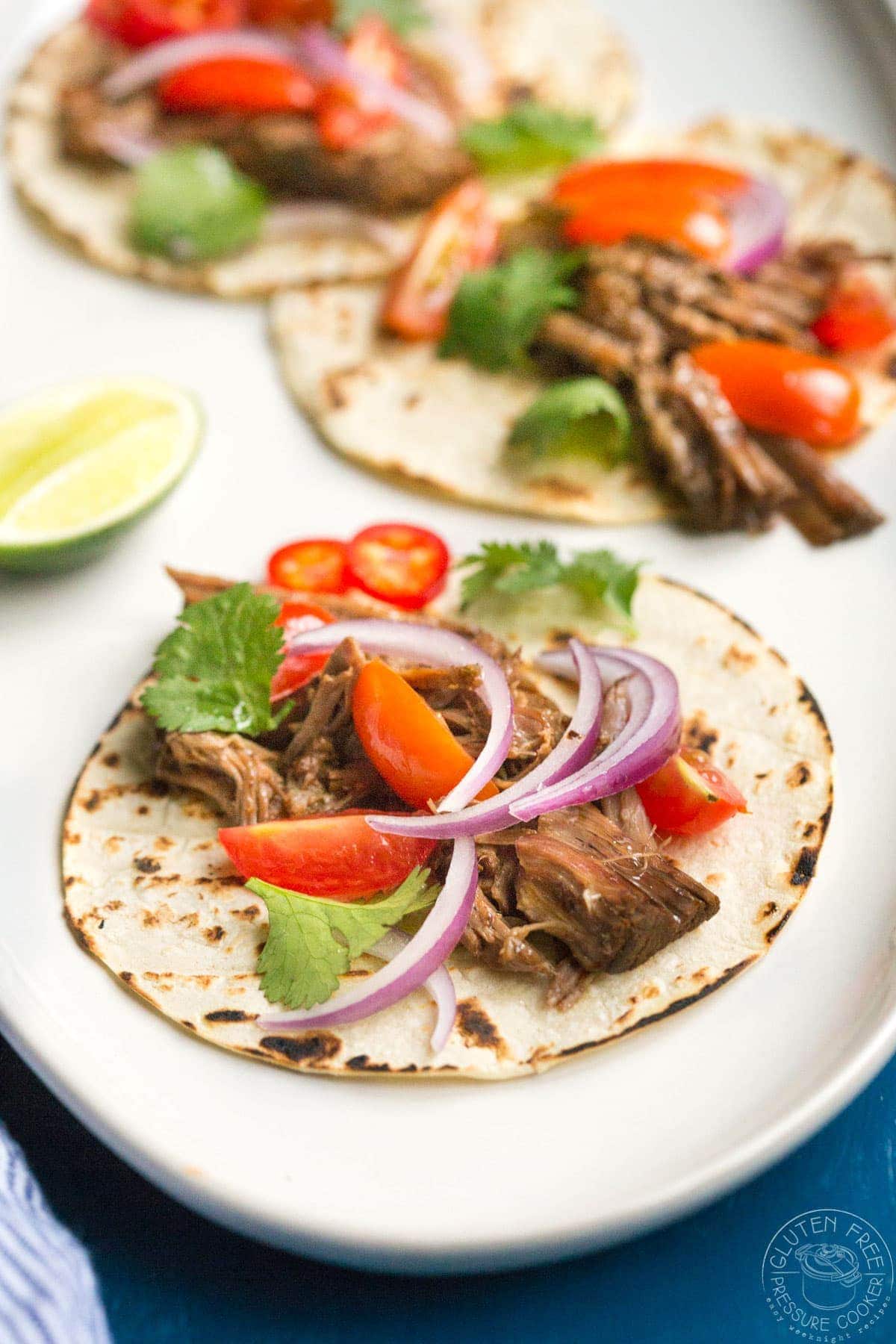 Barbacoa tacos with red onions and tomato on top