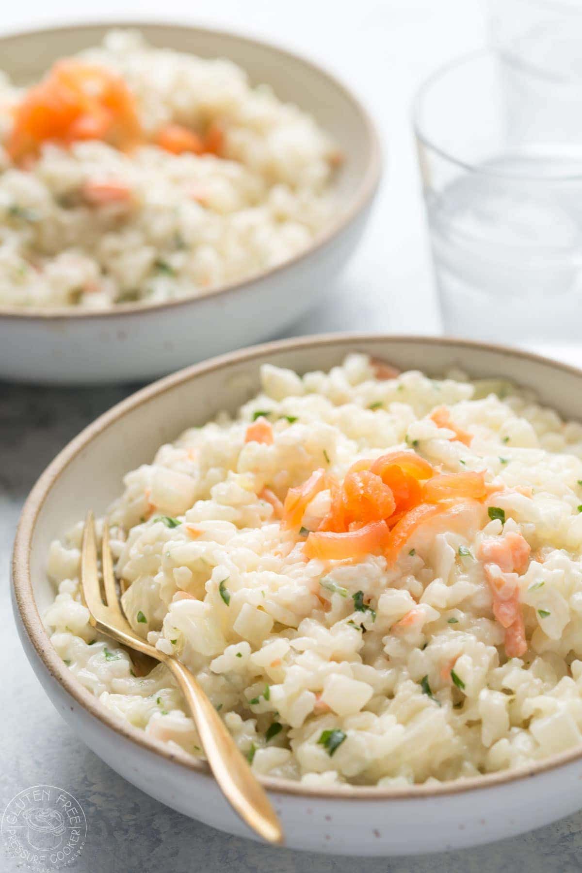 bowl of salmon risotto by a window with a glass of water