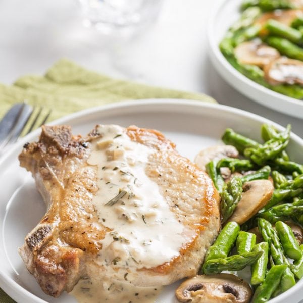 Cooked pork chop on a plate with asparagus and mushrooms