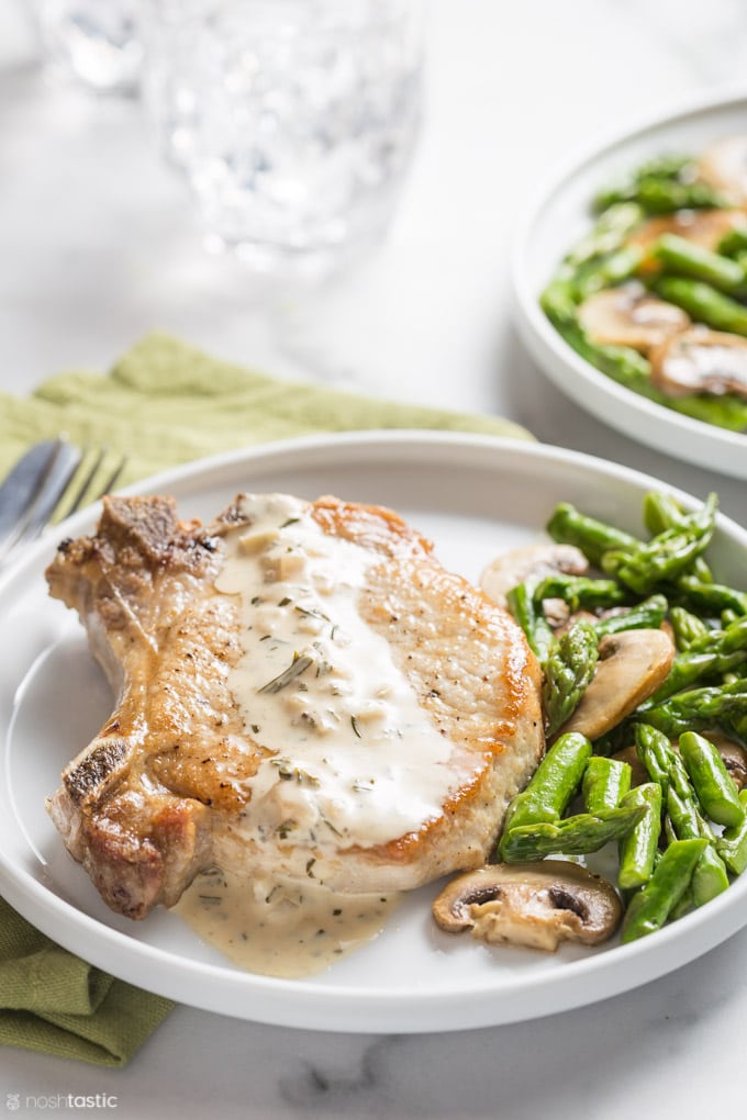 Cooked pork chop on a plate with asparagus and mushrooms