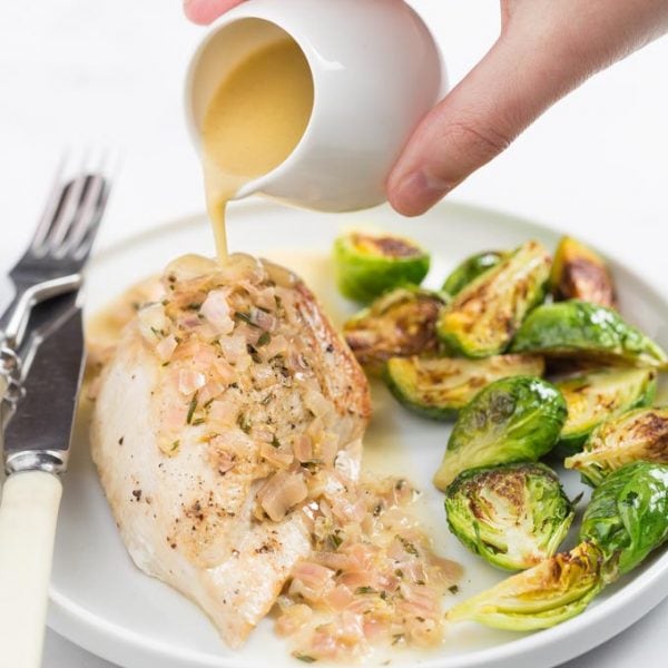 Chicken breast on a plate with lemon sauce pouring over the top