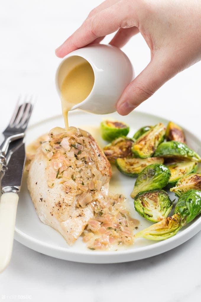 Chicken breast on a plate with roasted brussels sprouts and a sauce being poured over chicken