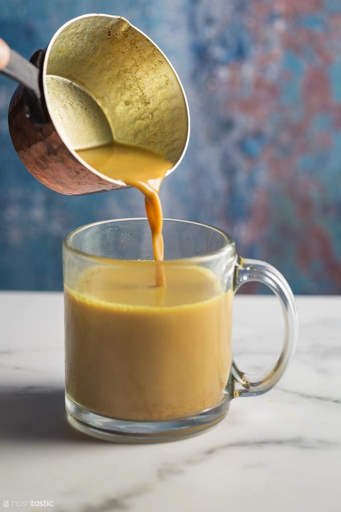 pouring turmeric tea from a pan into a mug
