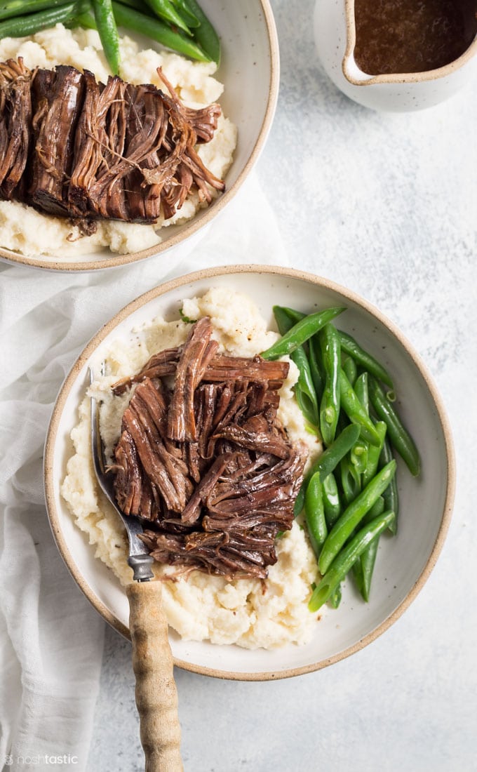 pot roast in a bowl with mashed cauliflower and green beans on a white table