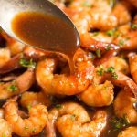 spooning honey garlic sauce over cooked shrimp