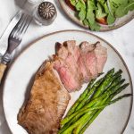 Sliced steak on a plate with asparagus and side salad