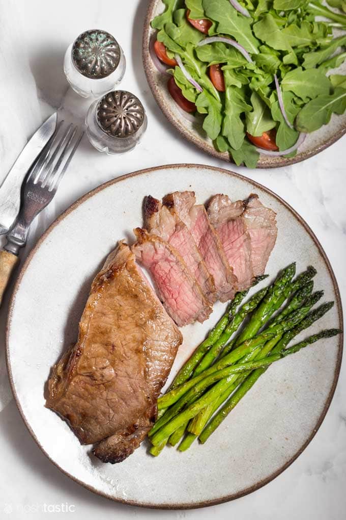 Sliced steak on a plate with asparagus and side salad