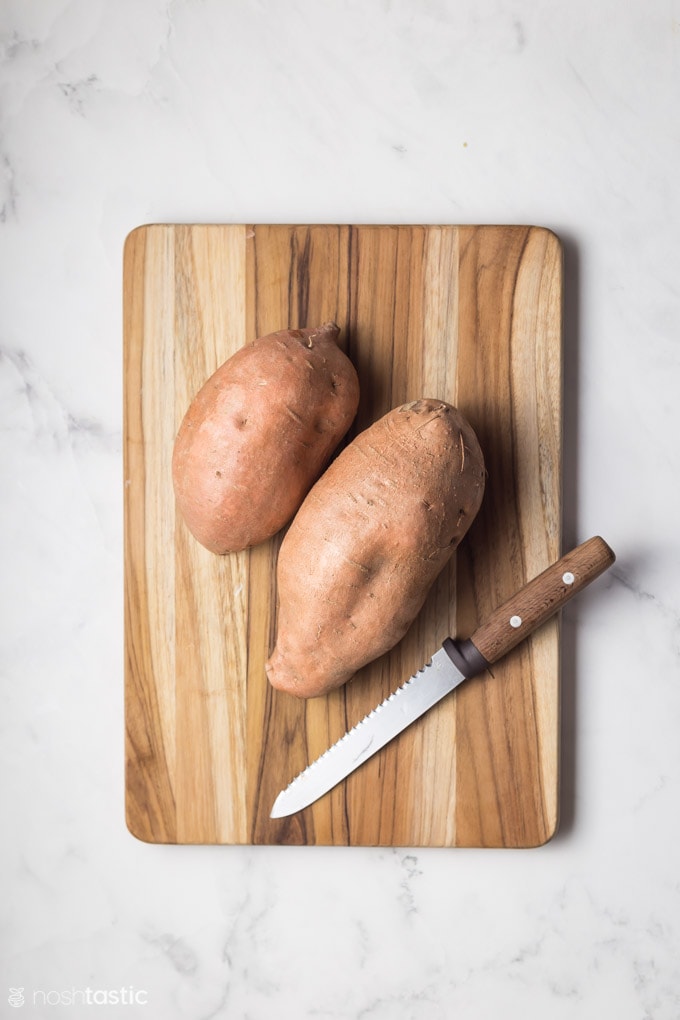 two sweet potatoes on a board with a knife