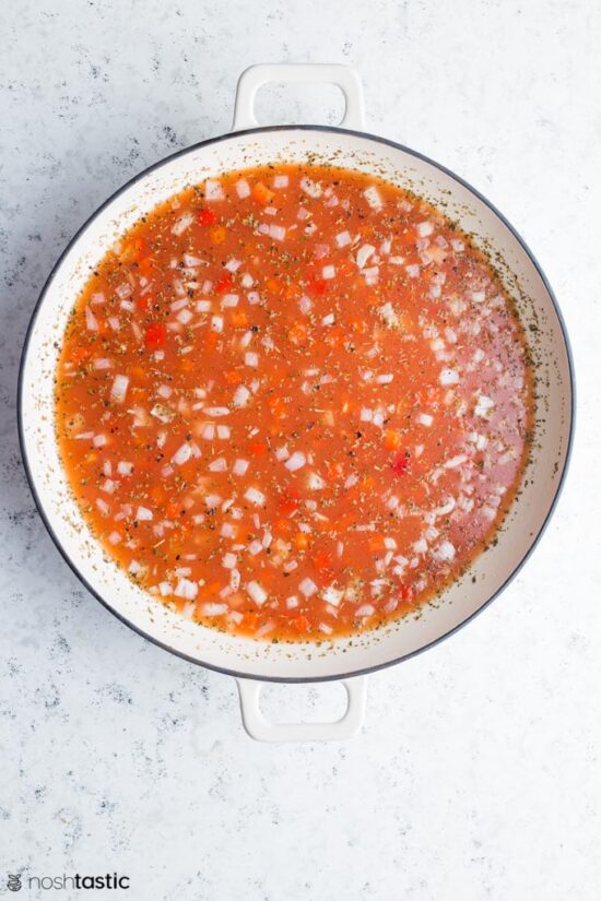 Rice, peppers, onion, and tomato broth in a pan