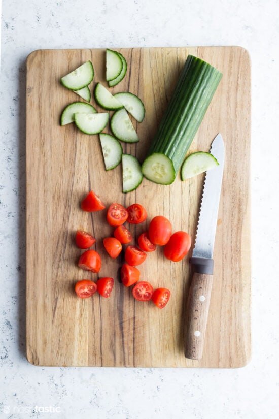 Tomatoes and cucumber slices with a knife on wooden board