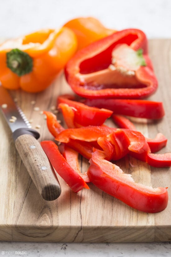 sliced red bell peppers on wooden board with knife