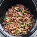 barbacoa beef in a slow cooker with cilantro garnish