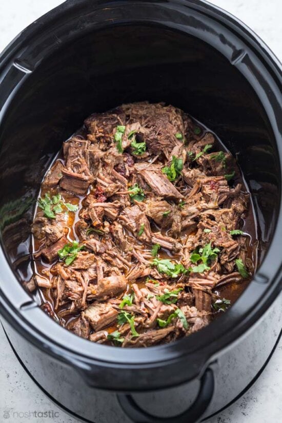 barbacoa beef in a slow cooker with cilantro garnish