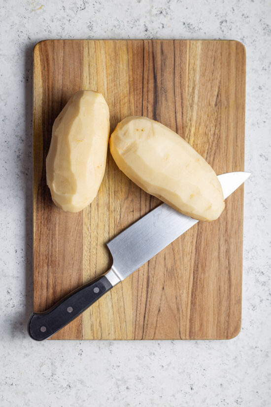 two potatoes and knife on board